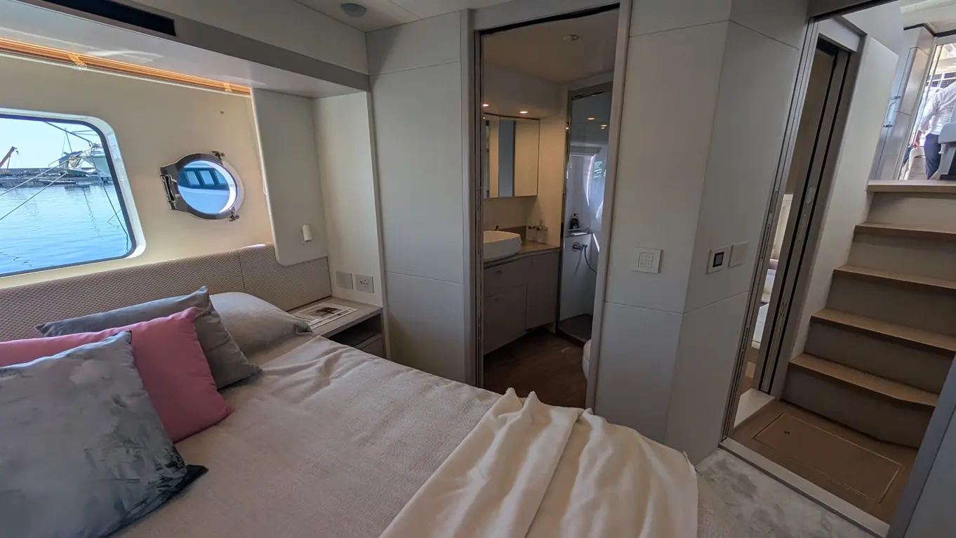 Elegant cabin interior with a bed, pillows, and an adjoining bathroom visible through a doorway; circular window overlooks water.